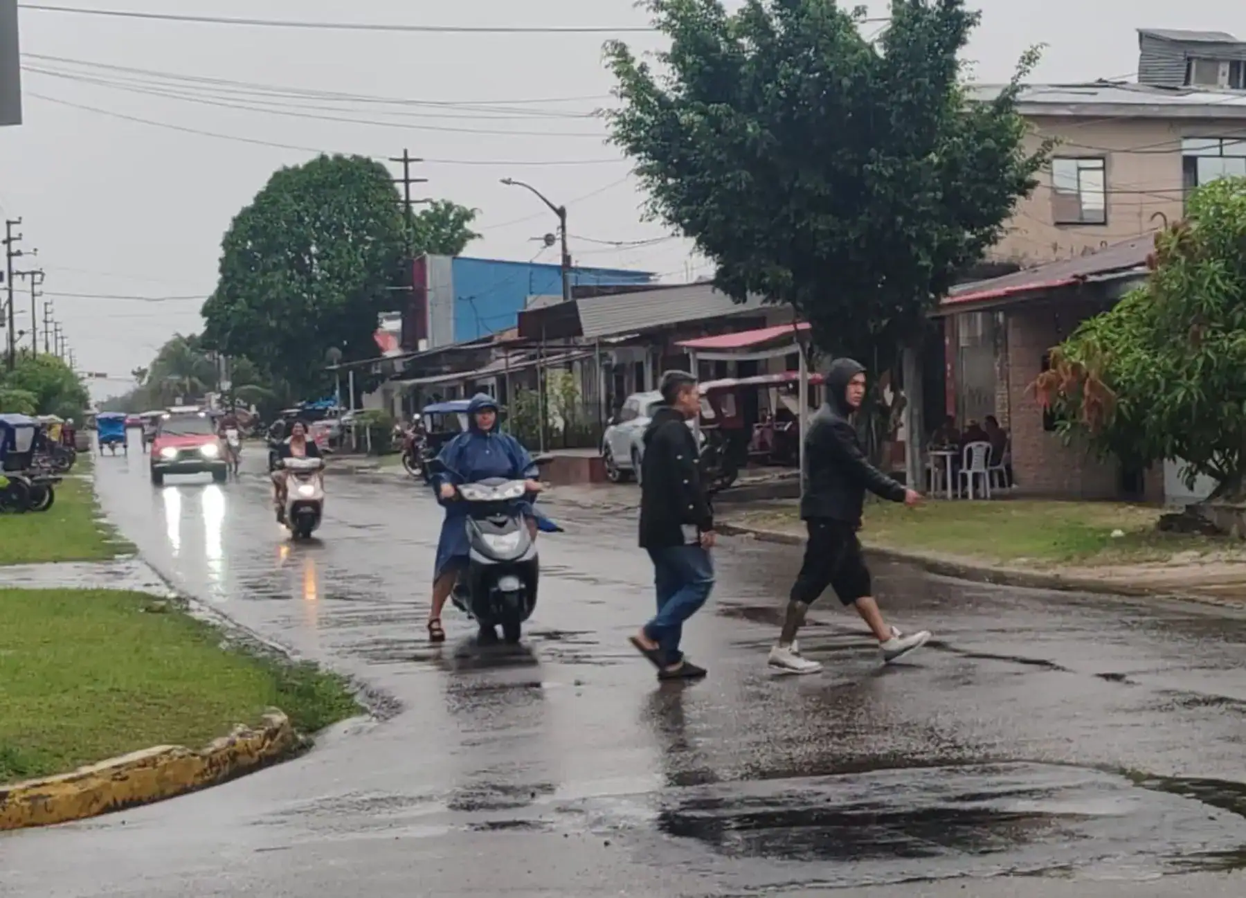 Persona cruzando la calle bajo la lluvia en Loreto, Perú, con motos y autos en movimiento, en un día nublado y lluvioso.