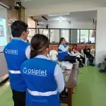 Infraestructura de capacitación en Loreto Noticias, con personal de Osiptel brindando información sobre regulaciones de telecomunicaciones a la comunidad local en un entorno escolar.
