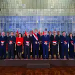Funcionarios y autoridades en ceremonia oficial en Loreto Noticias, usando bandas y trajes formales en un acto cívico en un auditorio institucional.