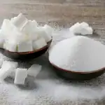 Azúcar blanca en cubos y azúcar en polvo en tazones, ingredientes utilizados en repostería y postres, en un fondo de mesa de madera.