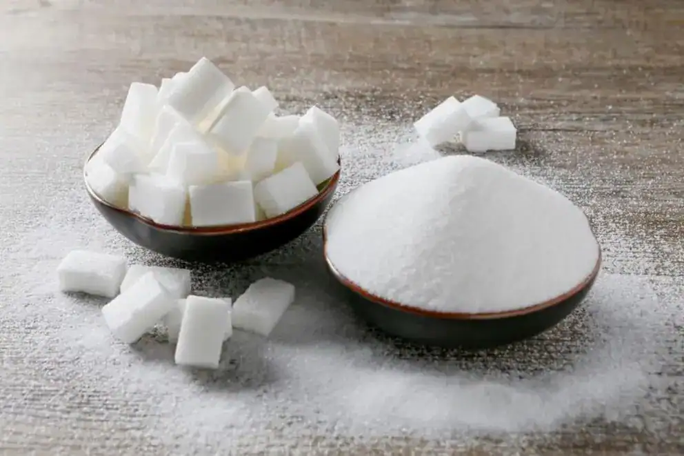 Azúcar blanca en cubos y azúcar en polvo en tazones, ingredientes utilizados en repostería y postres, en un fondo de mesa de madera.