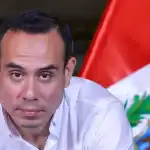 Diputado peruano en conferencia, frente a la bandera de Perú, discurso político, noticias de Loreto, escenario de autoridad, actualidad política peruana.
