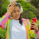 Nina con auriculares y teléfono móvil en un parque, mostrando incomodidad o frustración, en un entorno natural, resaltando temas de salud mental, estrés y tecnología en las noticias de Loreto Noticias.