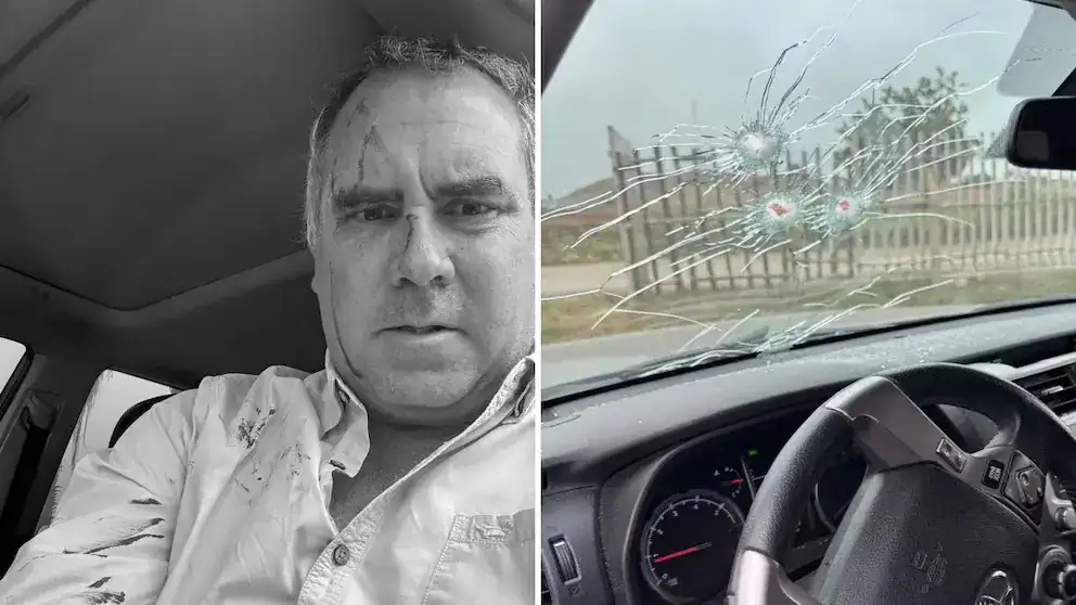 Alt text: Hombre con expresión de enojo y rostro agrietado por golpes, junto a vidrio de coche roto por impacto de balas.